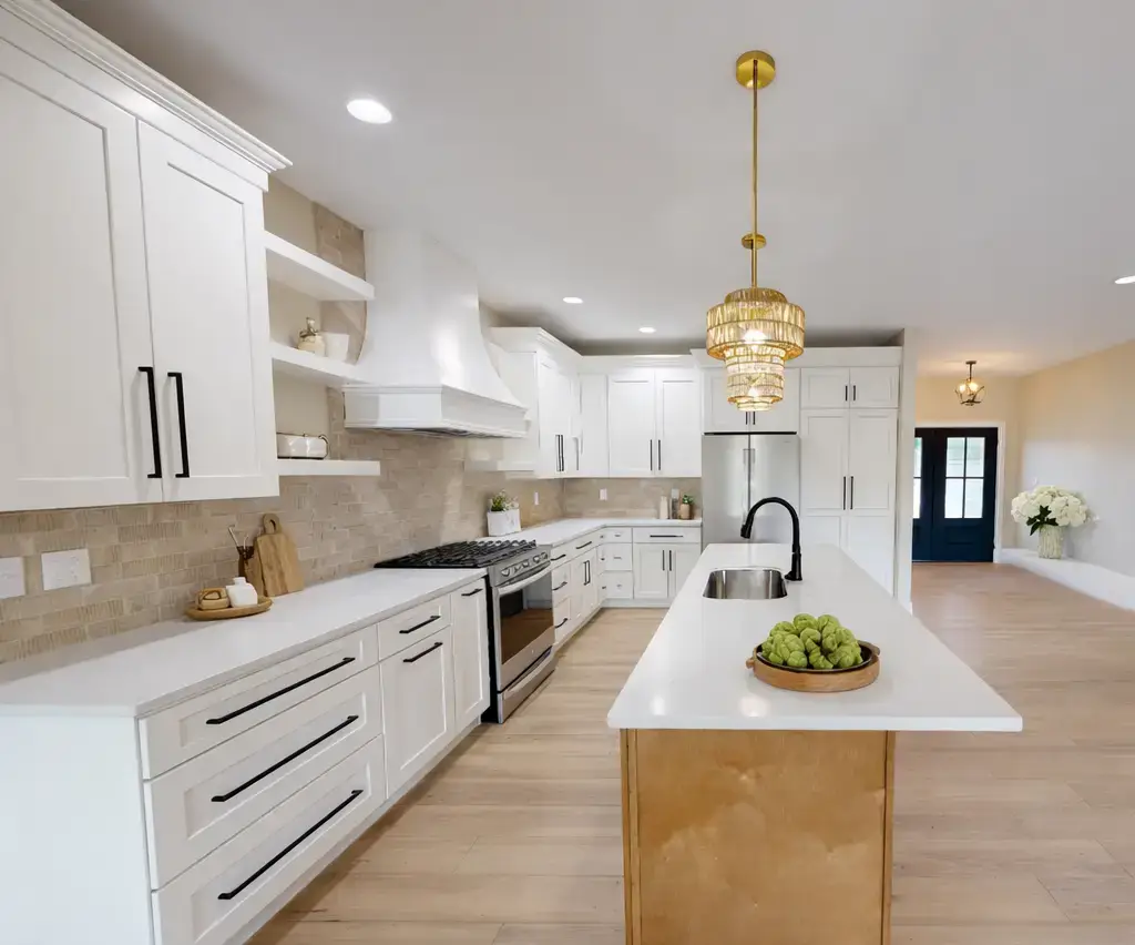 Modern kitchen with white cabinets, light wood flooring, a gold island with a sink, pendant lighting, stainless steel appliances, and a bowl of green apples on the counter—this move-in ready home for sale blends contemporary elegance with everyday functionality.