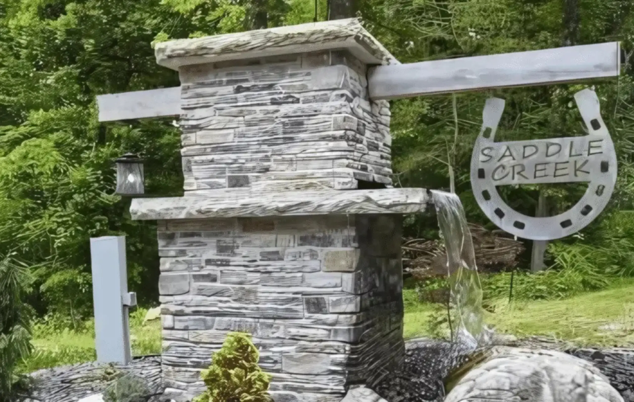 Saddle Creek Estates horseshoe entrance sign with stone pillar and woodland waterfall.